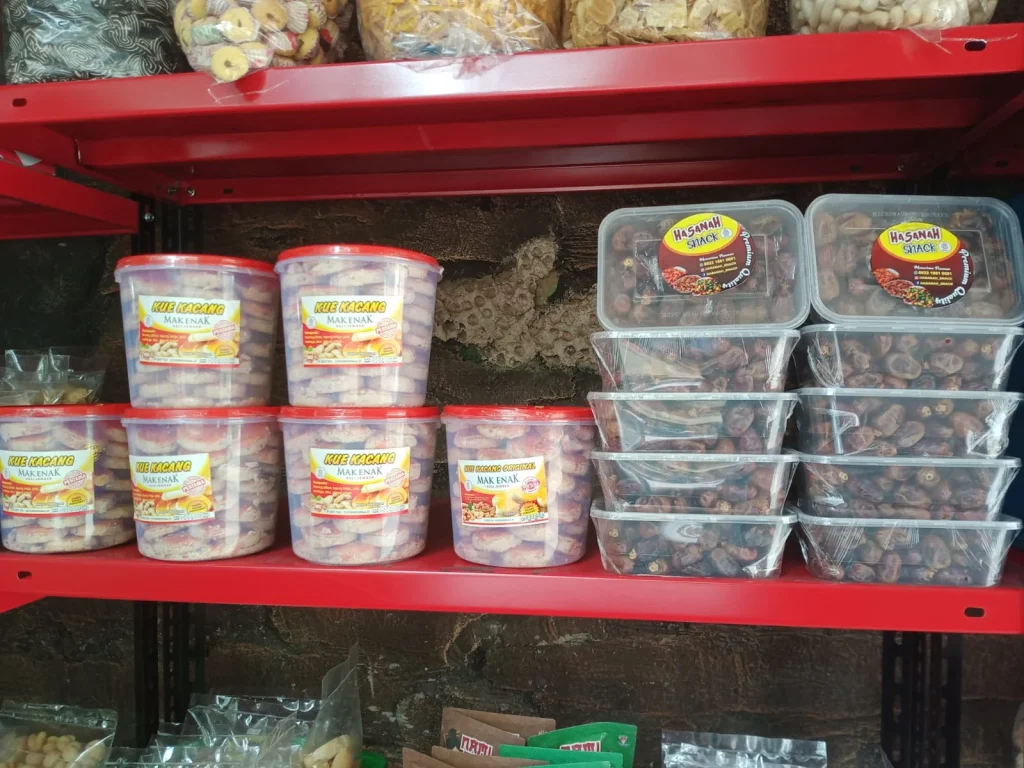 Etalase produk Hasanah Snack berisi kue kacang dalam toples dan kurma kemasan plastik higienis.