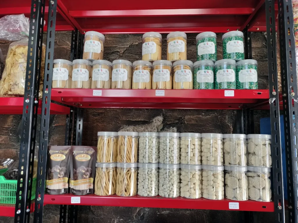 Etalase Hasanah Snack berisi berbagai kue kering, camilan stik, kacang berlapis, dan kurma coklat dalam kemasan toples higienis.